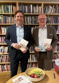 Herr Pleiner-Duxneuner, Geschäftsführer der AGES und Herr Ropin, Leiter des Fonds Gesundes Österreich stehen vor einem Bücherregal und halten die neue Broschüre in den Händen