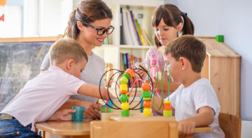 Kindergartenpädagogin mit drei Kindern an einem Tisch