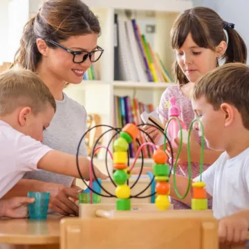 Kindergartenpädagogin mit drei Kindern an einem Tisch