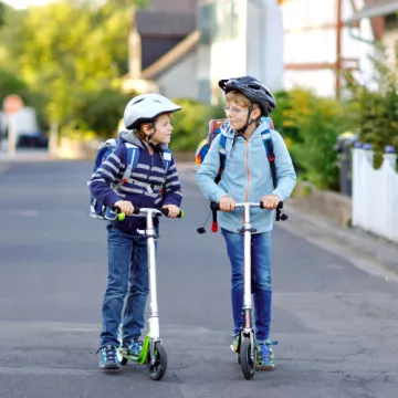 Zwei Kinder mit Tretrollern auf dem Schulweg