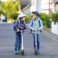 Zwei Kinder mit Tretrollern auf dem Weg zur Schule
