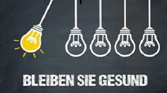 Eine leuchtende Glühbirne stößt andere nicht glühende an. Schriftzug darunter: Bleiben Sie gesund