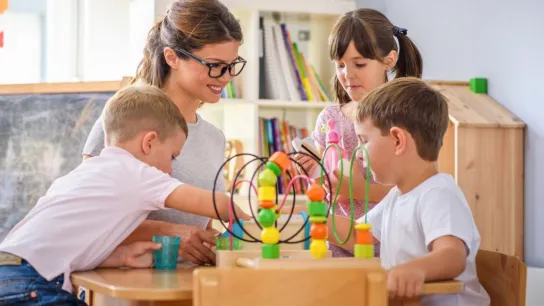 Kindergartenpädagogin mit drei Kindern an einem Tisch