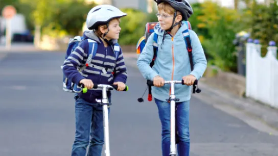 Zwei Kinder mit Tretrollern auf dem Schulweg